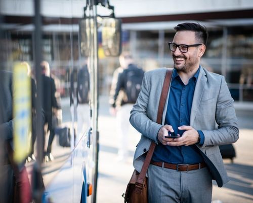 a smiling man walks next to a charter bus holding a briefcase